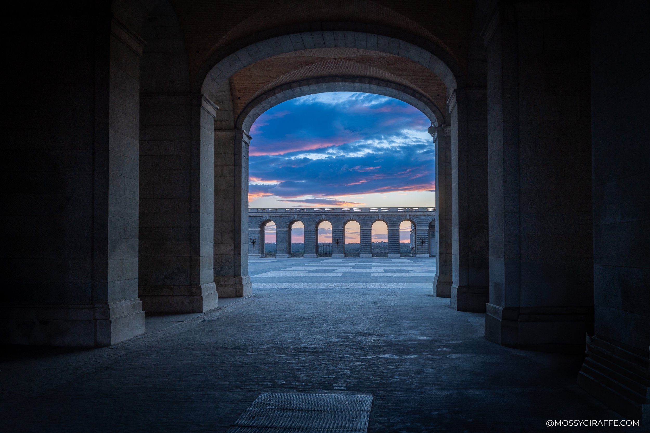 Sunset through a grand stone archway in Spain with pink and blue clouds over the courtyard